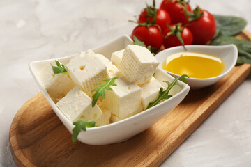 Bowl with cubes of feta cheese, arugula, cherry tomatoes and oil on grey background