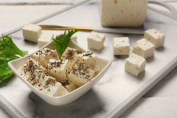 Board and bowl with cubes of feta cheese on white wooden background