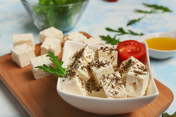 Bowl with cubes of feta cheese, spices, arugula and cherry tomato on light blue background
