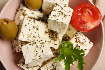 Bowl with cubes of feta cheese, spices, cherry tomato, olives and lettuce on napkin, closeup