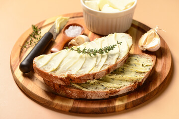 Wooden board of bread slices with fresh butter, garlic and salt on brown background
