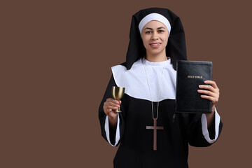 Portrait of young nun with Bible and chalice on brown background