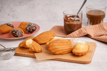 Wooden board with baking paper and delicious madeleines on white background