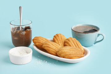 Plate with delicious madeleines, cup of coffee and chocolate paste on blue background