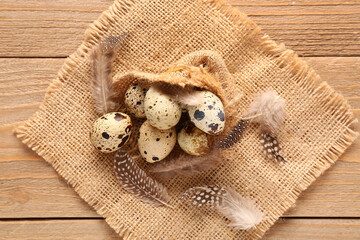 Burlap cloth with quail eggs and feathers on wooden background