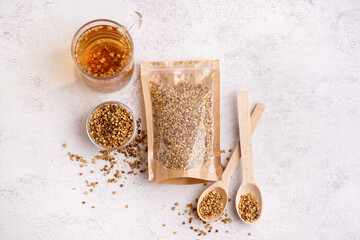 Pack with raw buckwheat, wooden spoons and glass cup of fresh tea on light background