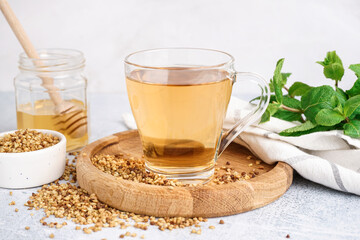 Glass cup of tasty buckwheat tea and mint on light background