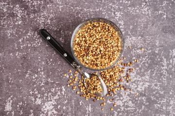 Glass with raw buckwheat grains and spoon on grey grunge background