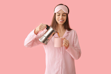Young woman in pajamas and mask holding cup and coffee pot on pink background