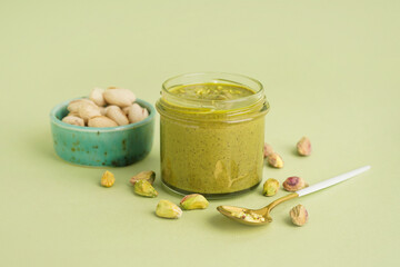 Tasty pistachio paste in jar and spoon on green background