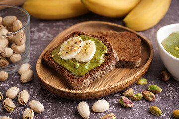 Wooden tray and pieces of bread with tasty pistachio paste on grey grunge background