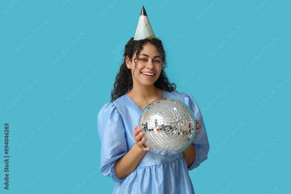 Wall mural Beautiful young African-American woman in party hat with disco ball on blue background