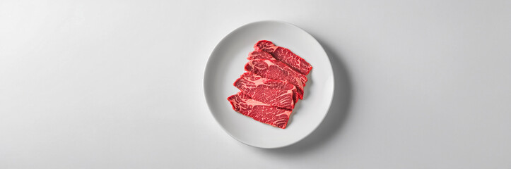 Obraz premium Raw beef steak slices arranged on a white plate, ideal for grilling or cooking a delicious meal