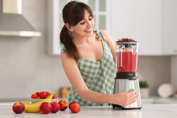 Young woman making delicious smoothie with blender at white marble table in kitchen