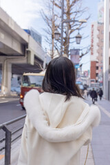 Twenty-something Chinese woman with black hair wearing a white coat with a fluffy fur hood and a white skirt walking on a public road in Minato, Tokyo, Japan.