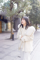 Twenty-something Chinese woman with black hair wearing a white coat with a fluffy fur hood and a white skirt walking on a public road in Minato, Tokyo, Japan.