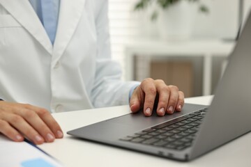 Doctor using laptop at white table in hospital, closeup