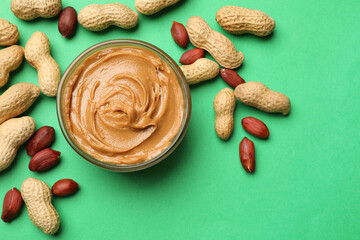 Tasty peanut butter in bowl and groundnuts on green background, flat lay