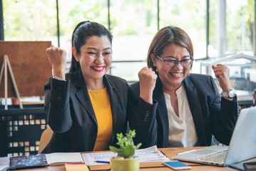 Happy success business woman partner working together in company office corporate executive teamwork. Meeting Executive Asian business woman using laptop office desk with fist arm raised win happiness