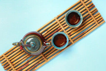 Bamboo mat with teapot and cups of tea on blue background