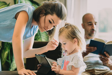 Young family relaxing at home enjoying digital tablet and book