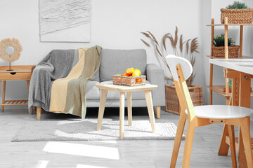 Wicker basket with citruses on coffee table near sofa in white living room