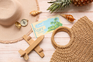 Composition with travel gift voucher, beach accessories and toy plane on light wooden background