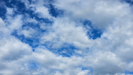 Background texture of white fluffy clouds in a dark blue sky in a 16_9 aspect ratio.