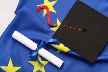 Diploma with blue ribbon and graduation hat on European Union flag