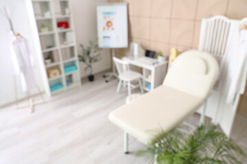Blurred view of medical office with couch, folding screen and doctor's workplace