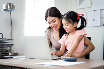 Young smiling asian  mother working from home using laptop computer while taking care of her little...