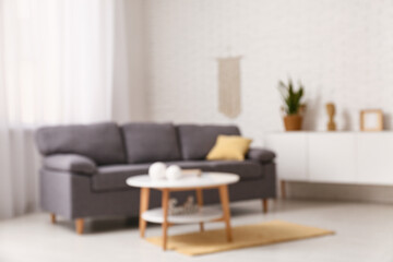 Cozy sofa with cushion and coffee table with book and decor in interior of living room. Blurred view
