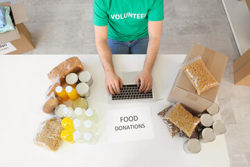 Male volunteer with food donations using laptop at table in center, top view