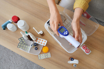 Woman putting infrared thermometer in first aid kit at home, top view