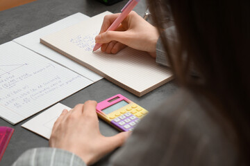 Woman writing math formulas in notebook at dark table, closeup