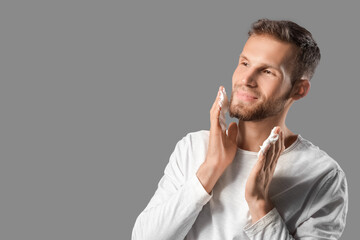 Bearded young man applying shaving foam on grey background