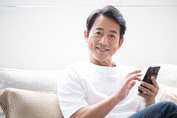 ソファに座ってスマホを操作する50代の男性　カメラ目線