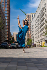 Beautiful Asian ballerina in blue dress posing in splits outdoors. Urban landscape. Vertical photo. 