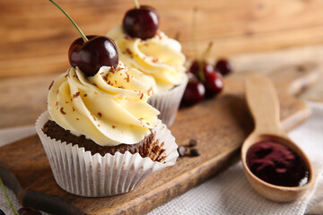 Board with sweet cherry cupcakes and spoon of jam on wooden background