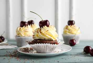 Plate with sweet cherry cupcake and berries on blue wooden table
