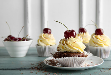 Plate with sweet cherry cupcake and bowl of berries on blue wooden table