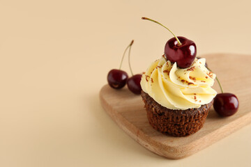 Wooden board with sweet cherry cupcake and berries on beige background