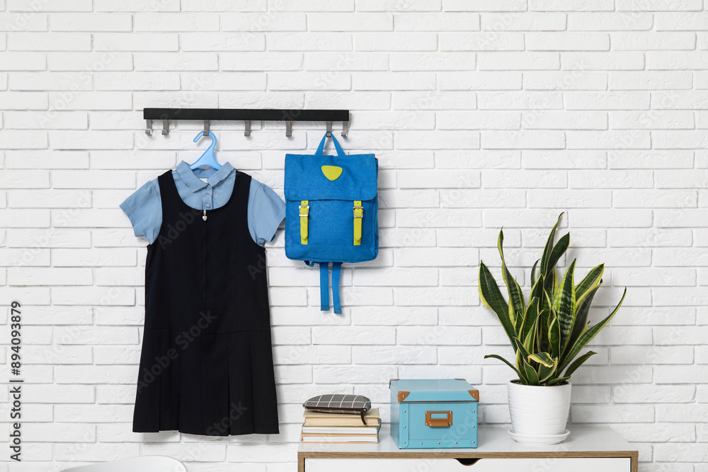 Wall mural Chest of drawers with stationery, houseplant and stylish school uniform hanging on light brick wall