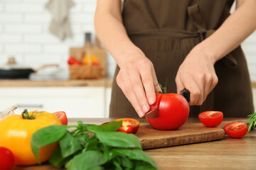 Woman cutting fresh tomato on wooden table in kitchen