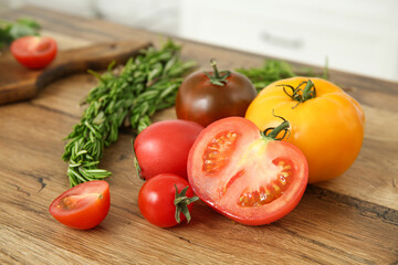 Different fresh tomatoes and rosemary on wooden table