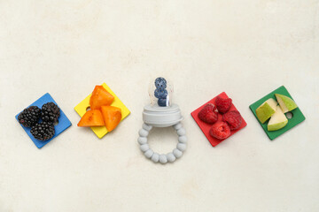 Composition with baby nibbler, fresh fruits and toys on light background