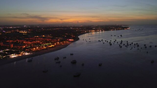Aerial view of Punta Cana, Dominican Republic, captured at dusk. The vibrant lights of the coastal town illuminate the shoreline, while the serene ocean reflects the hues of the setting sun.