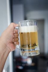 The person holding a beer cup with foam on top in the condominium on a sunny day
