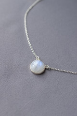 Shiny silver chain with moonstone on gray textile backgound. Elegant white pendant jewelry in minimalist style flat lay