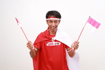 Fototapeta premium Excited Asian young boy with red white ribbon for celebrating Indonesia independence day standing while holding Indonesia flag